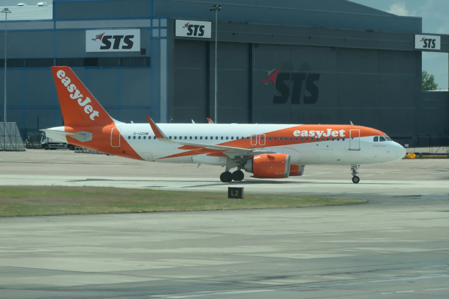 A white and orange easyJet Airbus A320neo airliner on the ground in front of a grey aircraft hangar
