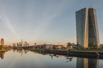 A twisting glass tower beside a calm river at dawn, with a cluster of skyscrapers in the distance