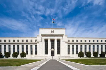 A wide white marble government building with tall columns at its entrance, a flag on the roof and a blue sky