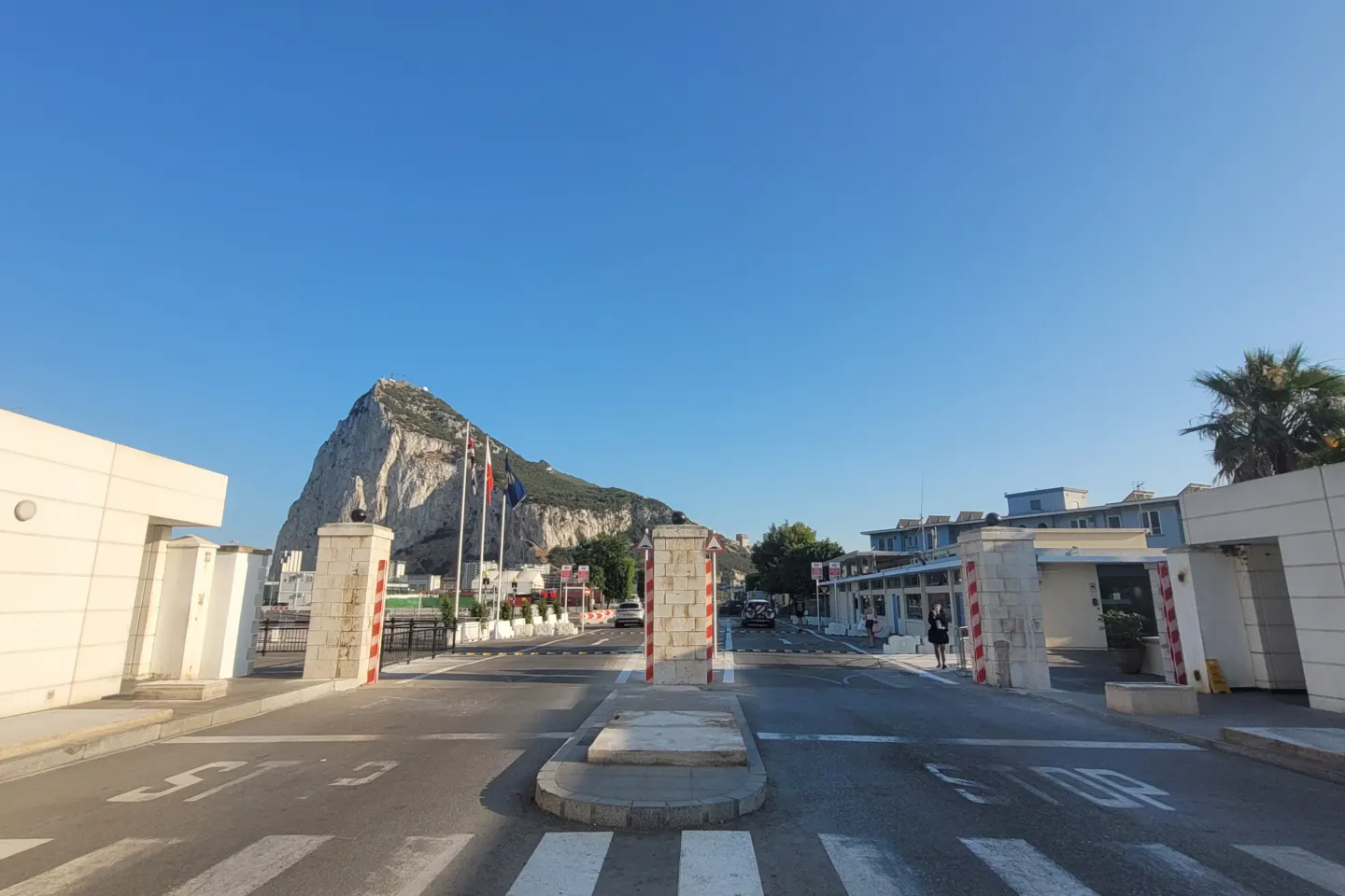 Empty road and pedestrian crossing at the Spain–Gibraltar frontier, with the Rock of Gibraltar behind low white buildings