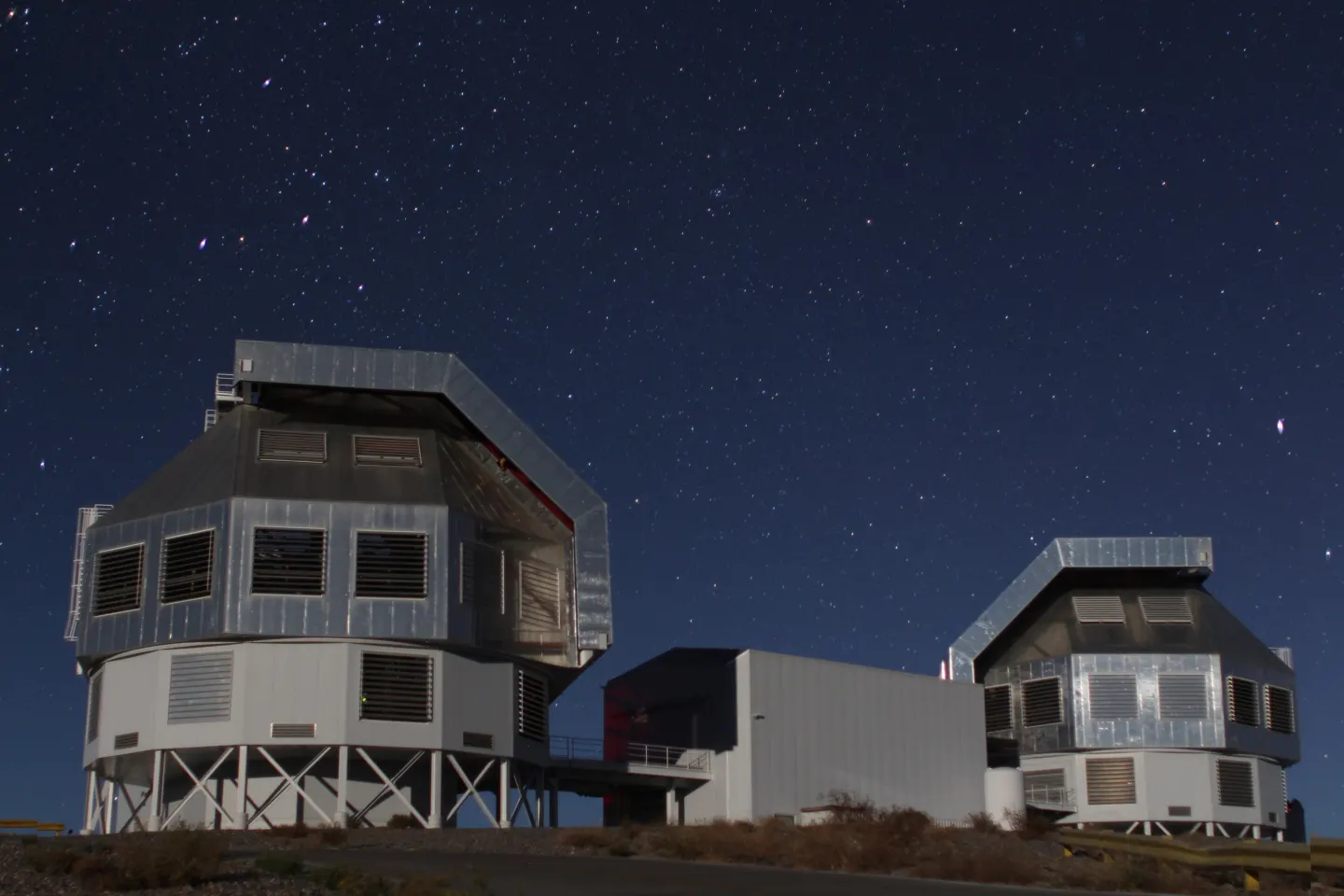 Two telescope domes on a desert ridge at night under a star-filled sky
