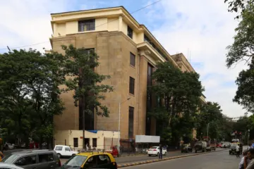 A sand-coloured stone office building several storeys high on a tree-lined city street with parked cars