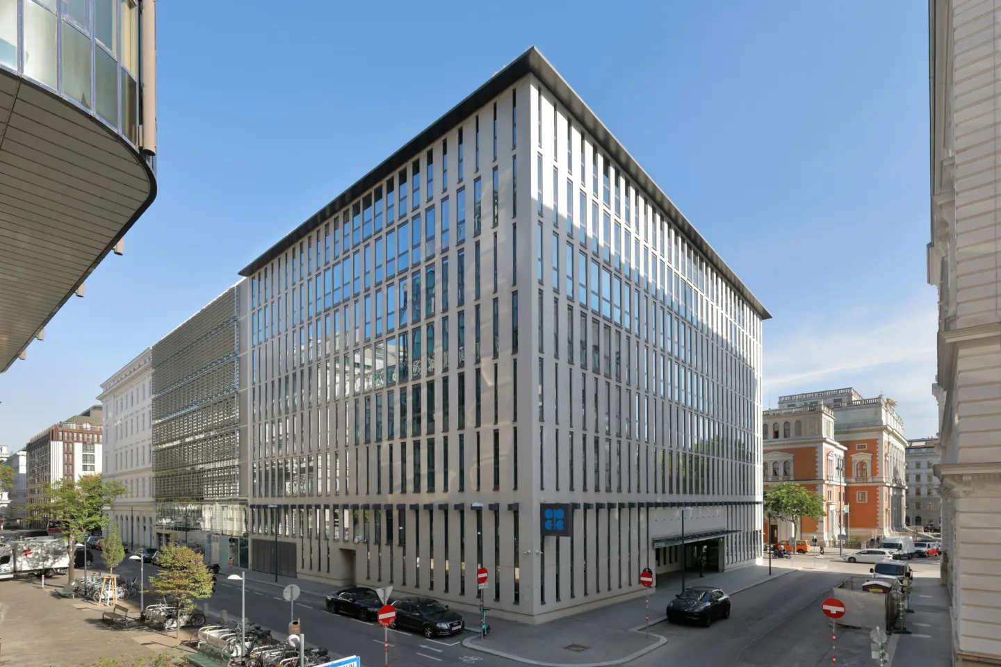 A modern glass and steel office building on a city street corner under a clear blue sky