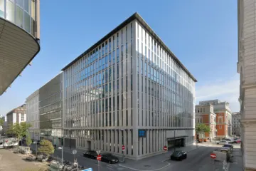 A modern glass and steel office building on a city street corner under a clear blue sky