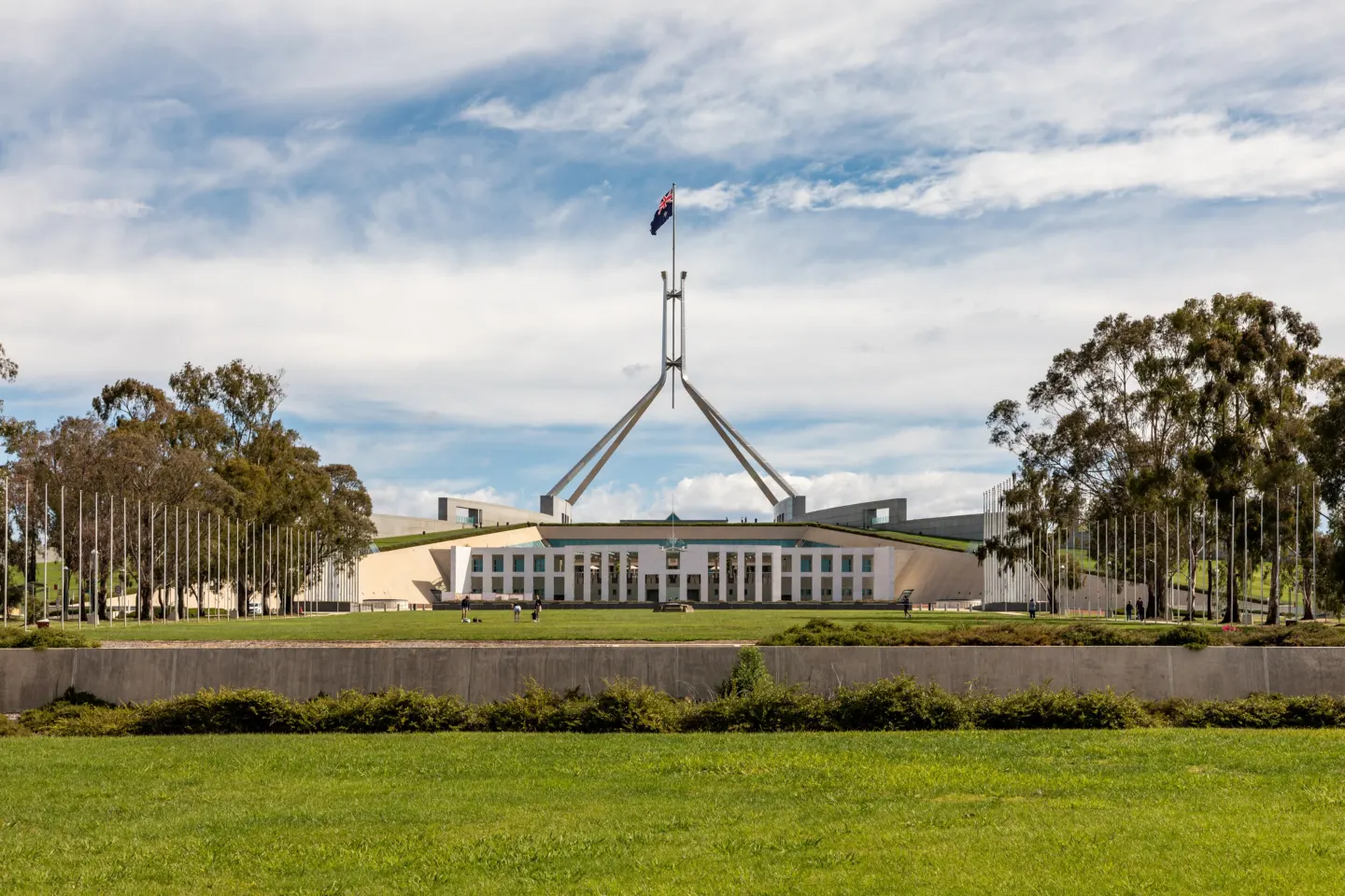 A wide, low white building with a tall flagpole flying the Australian flag, seen across green lawns