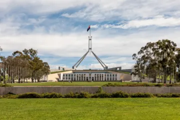 A wide, low white building with a tall flagpole flying the Australian flag, seen across green lawns