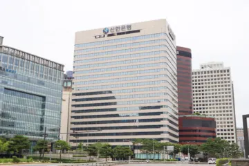 A beige high-rise office tower with Korean lettering on its top floor, flanked by other city buildings