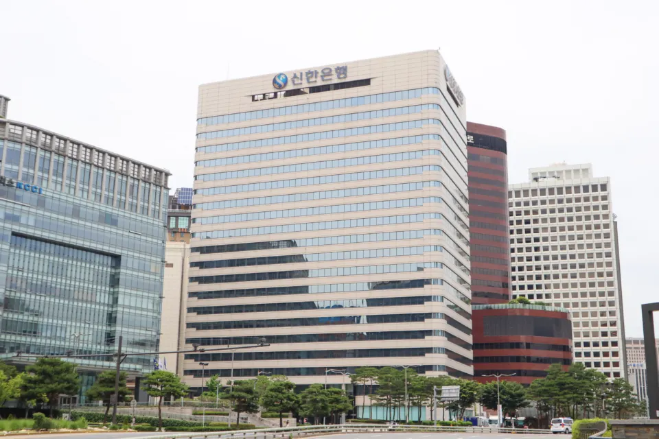 A beige high-rise office tower with Korean lettering on its top floor, flanked by other city buildings