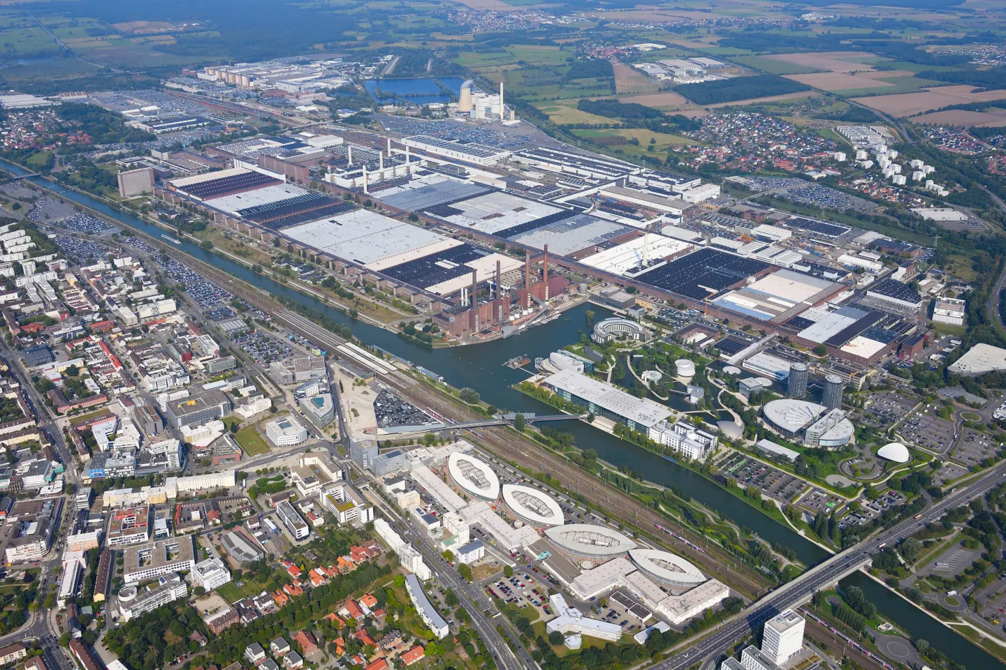 Aerial view of a vast factory complex beside a canal, surrounded by a town and fields
